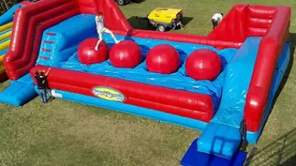 Red and blue inflatable obstacle course with large red balls and two people on a grassy field.