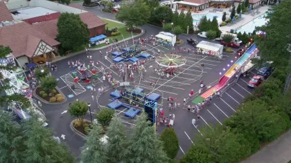Aerial view of a lively outdoor carnival with rides, games, and people gathered in a parking lot next to buildings.