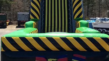 Colorful inflatable obstacle course with yellow and black stripes and green sections outdoors on a sunny day.