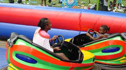 Two children enjoy riding colorful bumper cars at an outdoor amusement park with protective barriers.