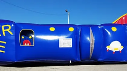 Blue inflatable lazer maze with colorful letters and cartoon eye and UFO designs on a sunny day.
