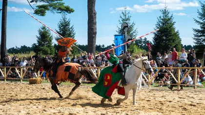 Two knights in colorful armor joust on horseback before a crowd at a medieval reenactment event.
