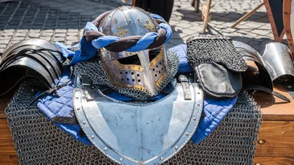Medieval knight armor including helmet, chainmail, and metal shoulder guards displayed on a wooden table outdoors.