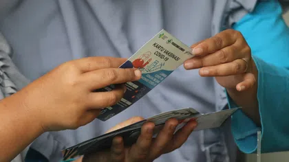 Close-up of hands exchanging a COVID-19 vaccination card with informational brochures in the background.