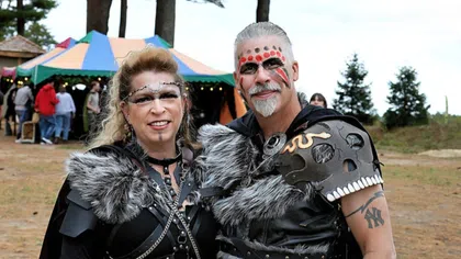 Couple dressed in Viking-inspired costumes with fur, face paint, and leather armor at outdoor festival.