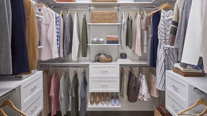Organized walk-in closet with hanging clothes, drawers, shelves, woven baskets, and shoes on a wooden floor.