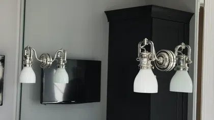 Modern bathroom sink with silver faucet, large mirror, dual wall lamps, and black cabinet reflected in mirror