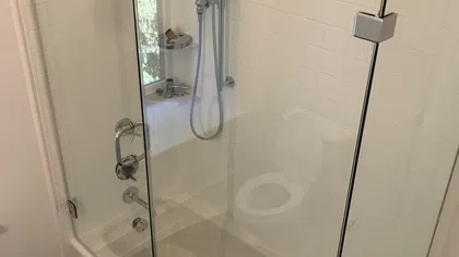 Modern bathroom with glass shower enclosure, white bathtub, and chrome shower fixtures and handle.