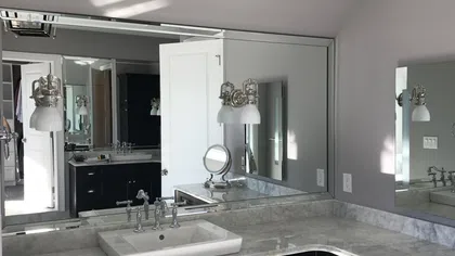 Modern bathroom with marble countertop, white sink, large mirrors, and wall-mounted light fixtures.