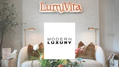 Cozy modern living room with white curved sofa, green and orange floral centerpiece, and LumiVita sign above.