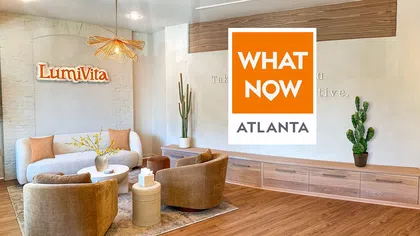 Modern living room with cozy furniture, wooden flooring, potted cacti, and Lumivita and What Now Atlanta logos on walls