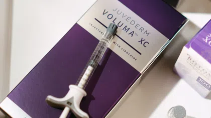 Close-up of Juvederm Voluma XC injectable filler box and syringe with lidocaine on white surface.