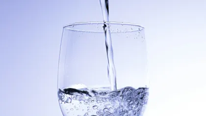 Clear water being poured into a wine glass against a light blue background with bubbles forming.