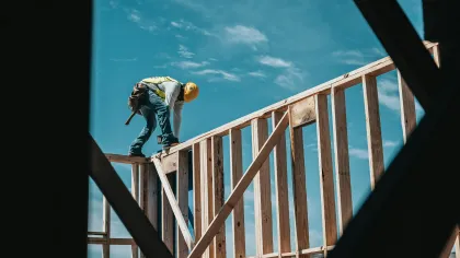 Construction worker in safety gear working on wooden house framing under blue sky