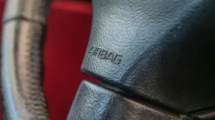 Close-up of a black leather car steering wheel featuring the word AIRBAG embossed on the center.
