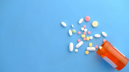 Various colorful pills spilling out of an orange prescription bottle on a blue background.
