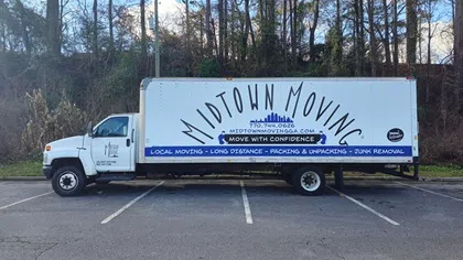 White Midtown Moving truck parked in an empty lot with trees in the background under a blue sky