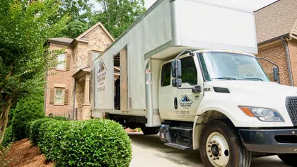 White Midtown Moving truck parked in driveway of a suburban brick house ready for moving service.
