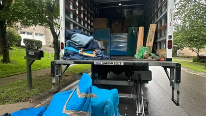 Open moving truck with wrapped furniture and blankets on a residential street near mailbox 4733 under green trees.