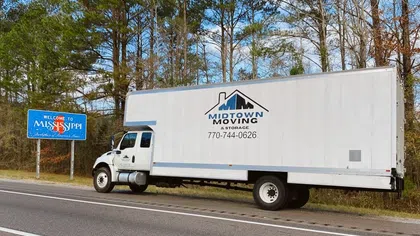 Midtown Moving truck parked beside Welcome to Mississippi sign on a highway with trees in the background.