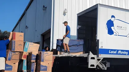 Moving truck being loaded with packed boxes by movers outside a warehouse on a clear sunny day
