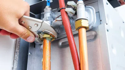 Hand tightening a pipe fitting on copper plumbing with an adjustable wrench, surrounded by pipes and valves