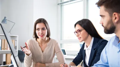 Three professionals discussing project data in a bright office while reviewing charts on a computer screen.