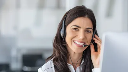 Smiling woman with headset working on computer in modern office, providing customer support or remote assistance.