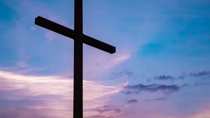 Silhouette of a large cross against a colorful sunset sky with purple and blue hues and scattered clouds