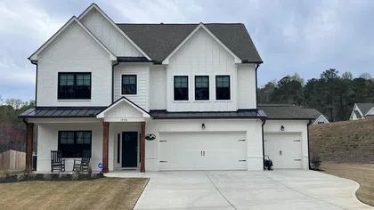 Modern two-story white house with black roof, double garage, front porch, and concrete driveway under cloudy sky.