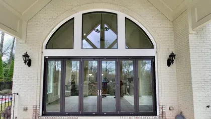 Arched glass double doors with black frames and side windows on white brick exterior wall under covered porch