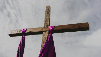 Wooden cross draped with a purple cloth against a cloudy sky symbolizing faith and spirituality.