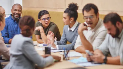 Diverse group of professionals engaged in a collaborative meeting around a table with papers and devices.