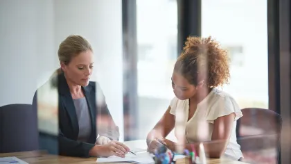 Two professional women discussing documents at a desk in a modern office setting.