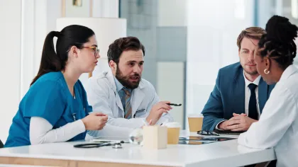 Medical professionals and businessperson discussing patient care around a table in a bright office setting.