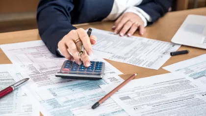 Person using calculator and pen to fill out tax forms and financial documents on a wooden desk