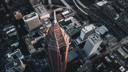 Aerial view of a cityscape featuring a prominent skyscraper surrounded by modern buildings and roads at sunset.