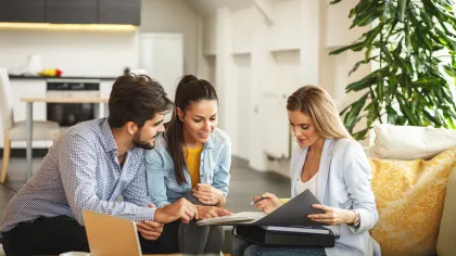 Couple consulting a female agent with documents in a modern living room setting during a financial meeting.