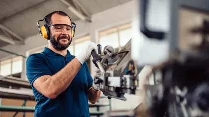 Manufacturing worker wearing safety gear operates industrial machinery in a factory setting with focused expression