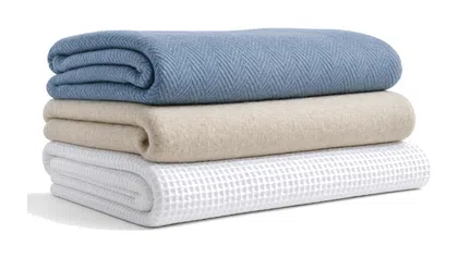 Stack of three folded blankets in blue, beige, and white waffle textures on white background.