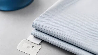 Close-up of a folded breathable fabric with a small electronic sensor tag attached on a gray surface.