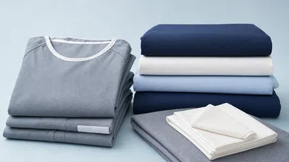 Neatly folded blue, white, and gray bedding and clothing stacked on a light blue surface.