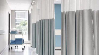 Modern hospital corridor with privacy curtains and a cart stacked with blue towels near a window.
