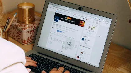 Person using a MacBook Air on a wooden desk with LinkedIn profile visible on screen and a candle nearby
