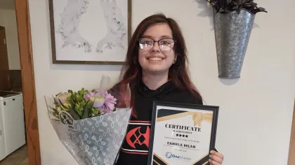 Two women smiling indoors, one holding a certificate of achievement, the other holding a gift bag.