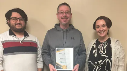 Two women smiling indoors, one holding a certificate of achievement, the other holding a gift bag.