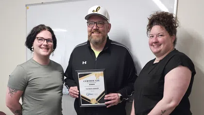 Three people standing in front of a whiteboard, with a man in the center holding a certificate and smiling.