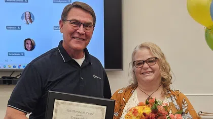 Man presenting award certificate to smiling woman holding a bouquet of flowers at indoor ceremony.