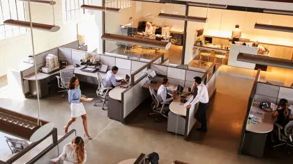 Modern office interior with employees working at desks and collaborating in a bright, open space.