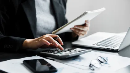 A business professional calculates finances with a calculator and reviews documents on a desk.